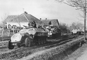 German armored vehicles advance down muddy road during Operation Spring Awakening.